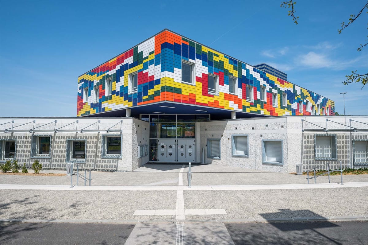 École neuve aux façades multicolores, parvis dégagé devant l'entrée