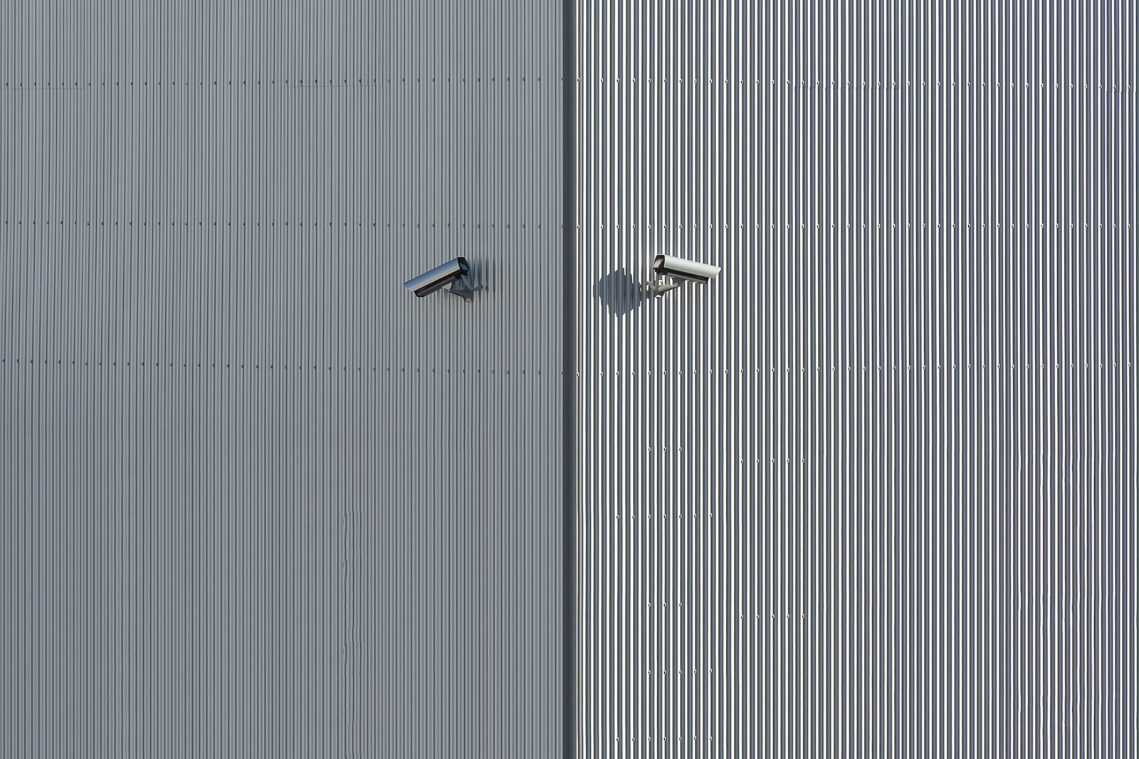 Deux caméras de vidéosurveillance posées sur le bardage métallique d'un bâtiment tertiaire